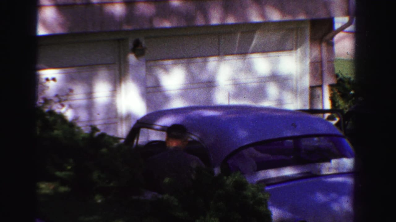 Man near a blue sedan parked in front of a white garage.