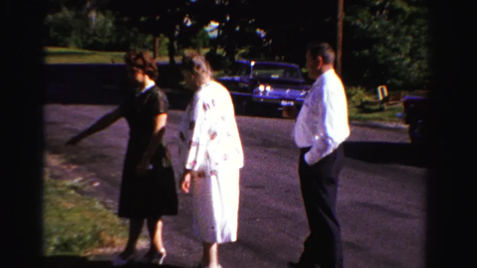 Three adults converse on a suburban Ontario driveway, with parked cars and trees visible behind them.