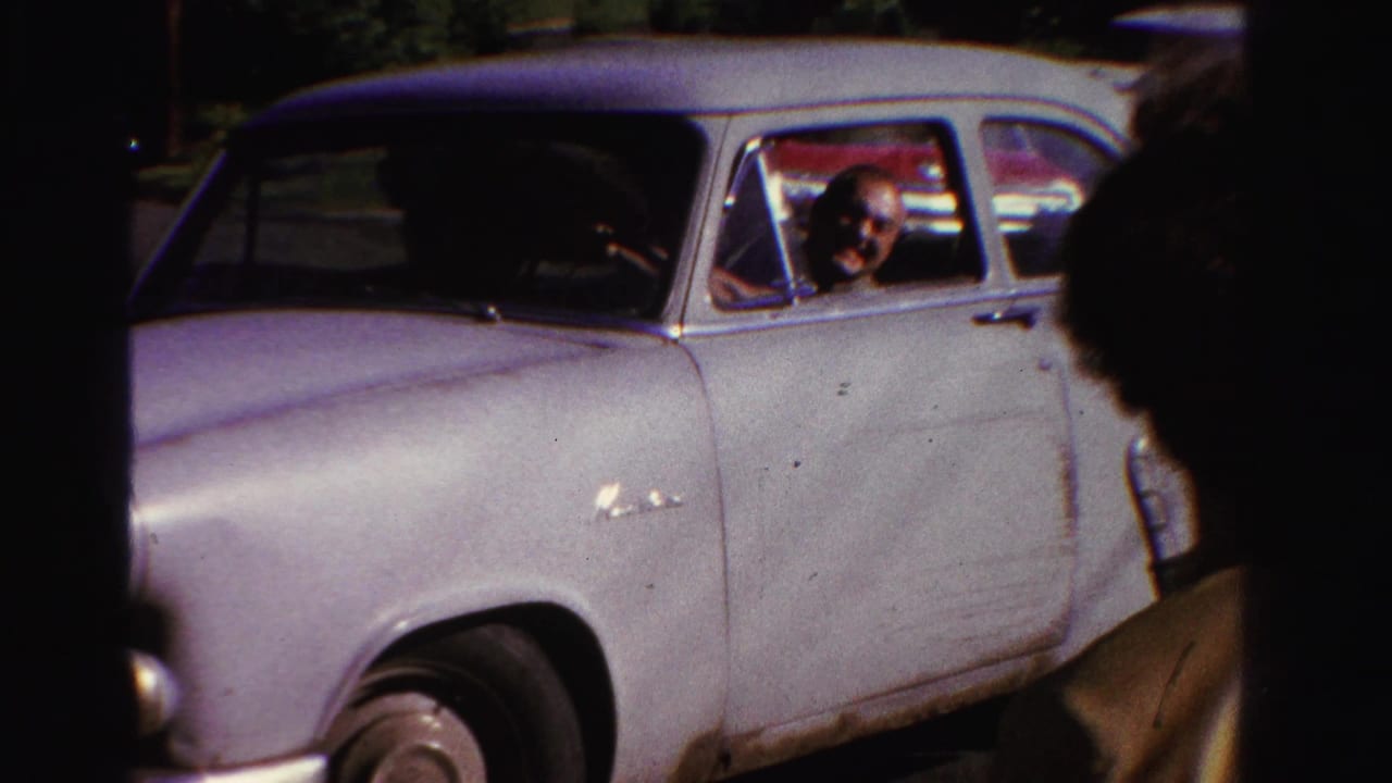 1958 Ontario 8mm frame showing a pale classic sedan in a parking area, with the driver visible through the open side window.