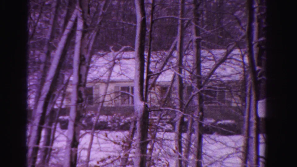 1958 Ontario 8mm view of a snow-covered house glimpsed through leafless trees in a winter wooded setting.