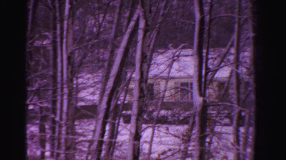 1958 Ontario home-movie frame showing a snow-covered house through winter trees, with dark film edge visible.