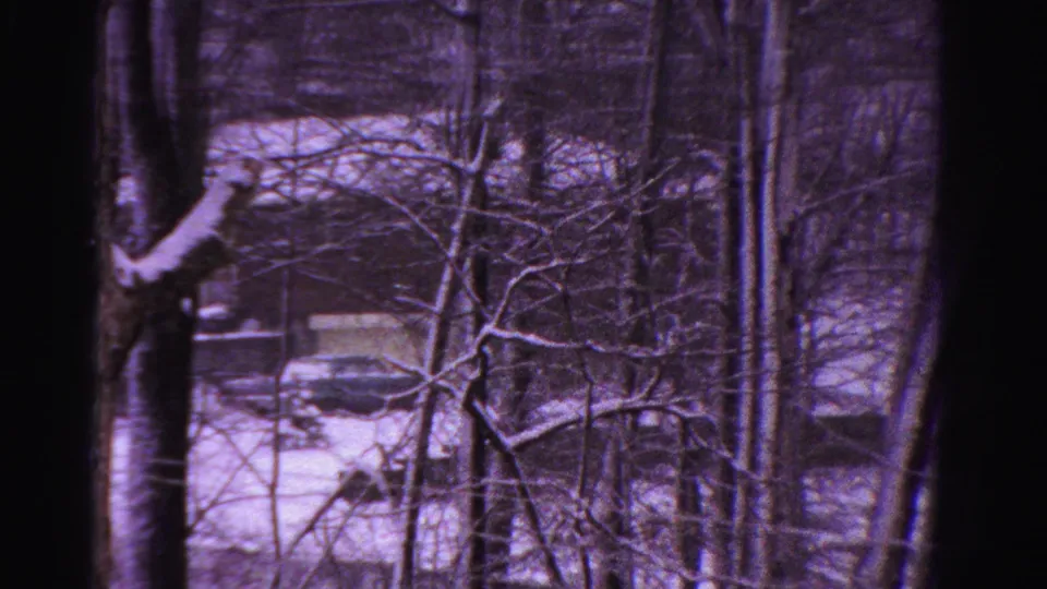 8mm home-movie frame from 1958 Ontario showing a wooded snowy foreground and a partially visible car near a house.