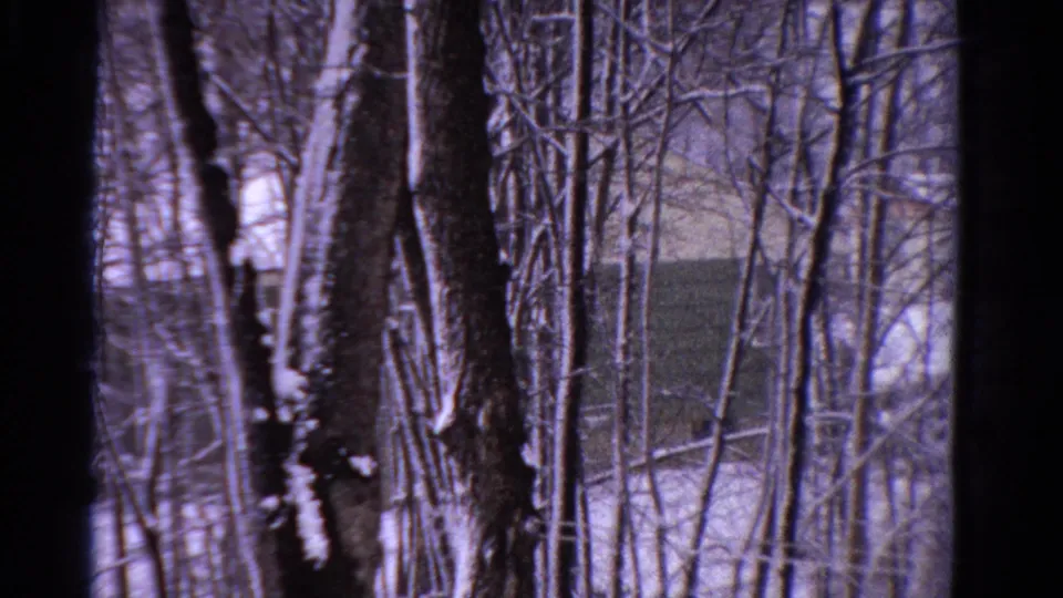 1958 Ontario 8mm frame showing winter woods, snow, and a partially obscured dark structure beyond the trees.