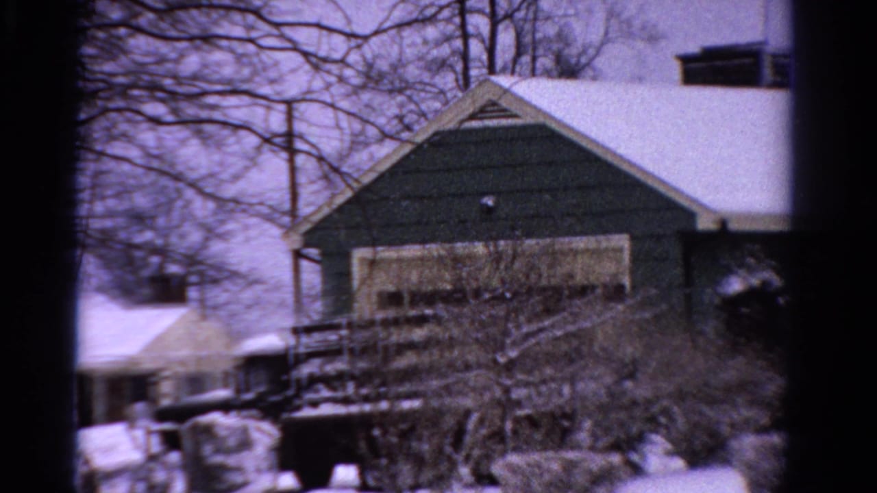 Snow-covered house and yard with bare trees and a dark truck nearby.