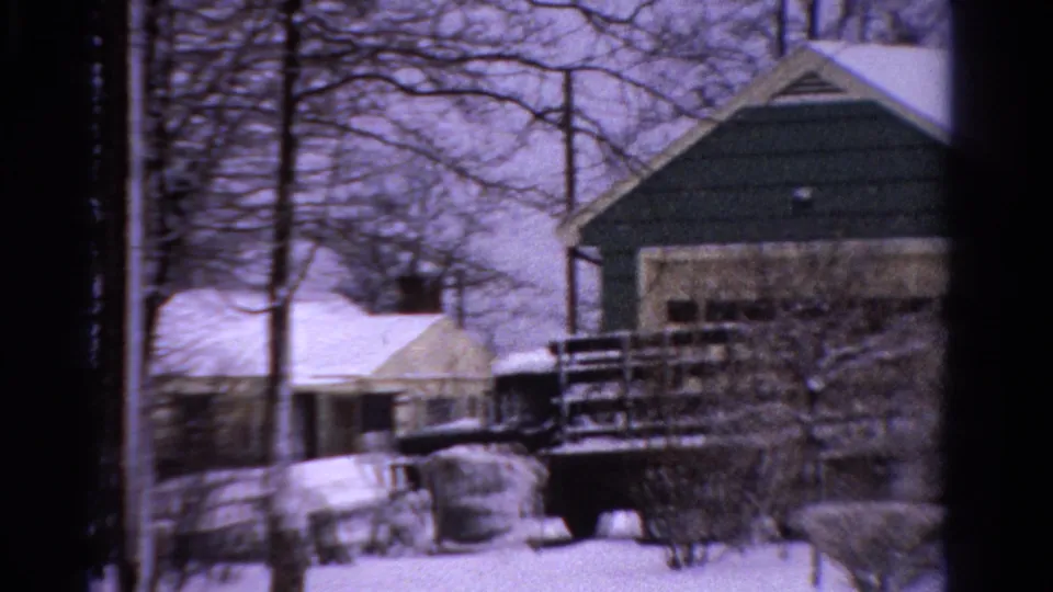 1958 Ontario winter frame with a snow-covered residential exterior, bare trees, shrubs, porch railing, and dark parked vehicle.