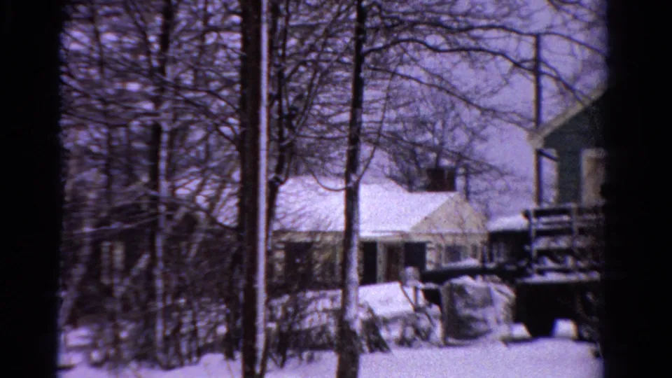 1958 Ontario home-movie frame showing a snowy residential street with houses, utility poles, bare trees, and a dark truck.