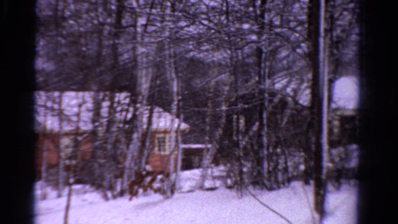 1958 Ontario 8mm frame showing a brown building with a snow-covered roof behind leafless trees.