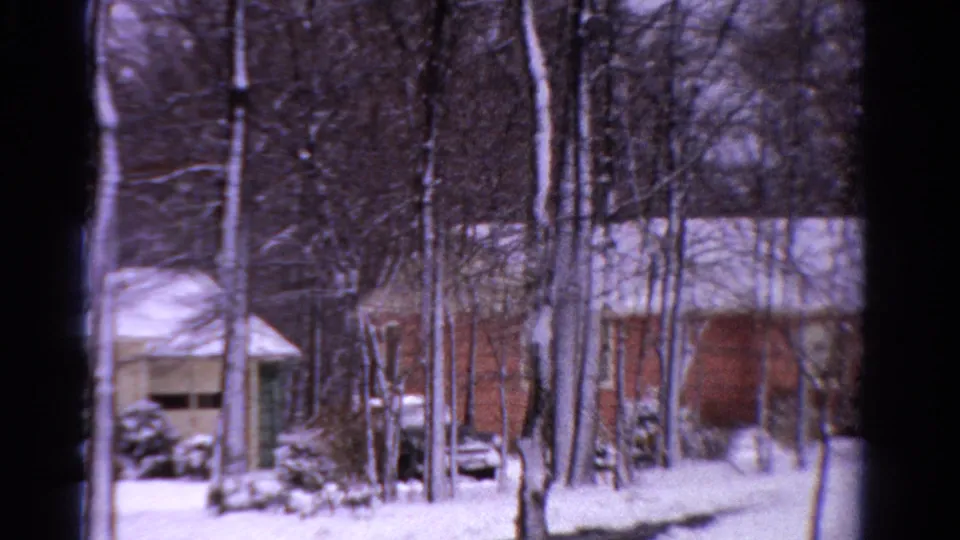 Ontario winter frame showing a tan garage-like structure, brown building, snow-covered roofs, bare trees, and a parked vehicle area.