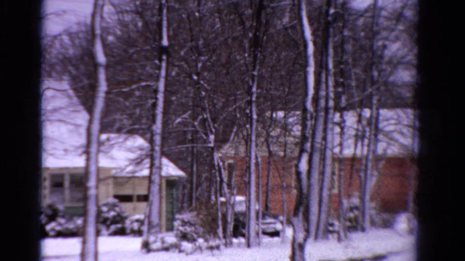 1958 Ontario home-movie view of a snow-covered suburban house framed by leafless trees and a dark window edge.