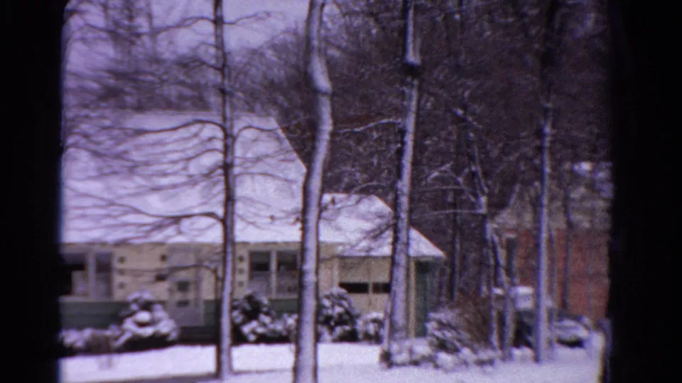 1958 Ontario winter view of a modest suburban house, snow-covered shrubs, and leafless trees from a home-movie perspective.