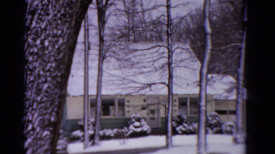 A 1958 Ontario snowy neighborhood view with a large tree trunk, bare branches, and a modest house beyond.
