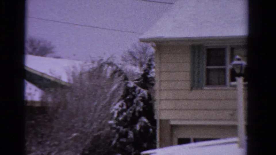 1958 Ontario home-movie frame showing a house corner with a window, snowy roofline, evergreen, and bare winter trees.