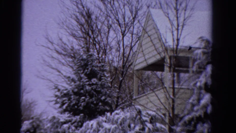 1958 Ontario 8mm frame with a house exterior, snow-covered shrubs, bare trees, and a pale overcast winter sky.