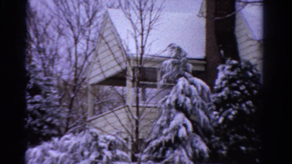 Snow-covered shrubs and bare trees stand before a pale suburban house in Ontario, captured on 8mm film in 1958.