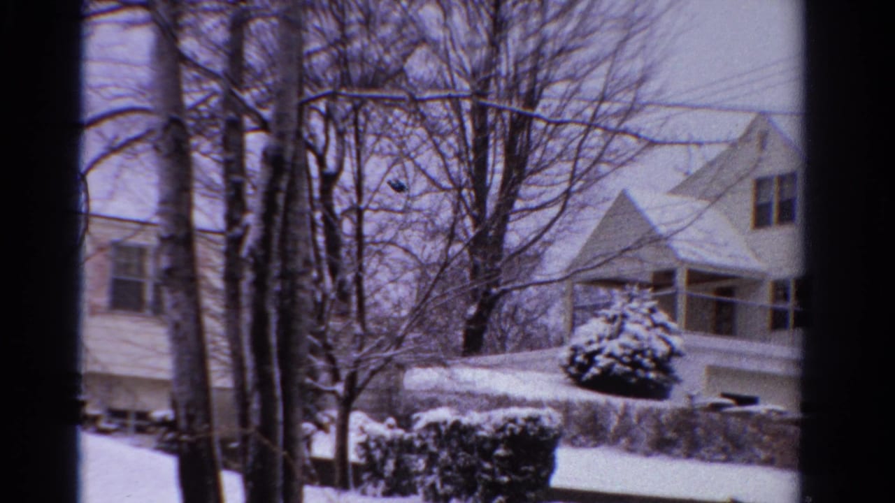 Snowy suburban house and yard framed by bare trees and dark film edges.