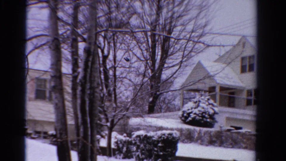 1958 Ontario 8mm frame showing a snow-covered suburban house, shrubs, bare trees, and winter street frontage.