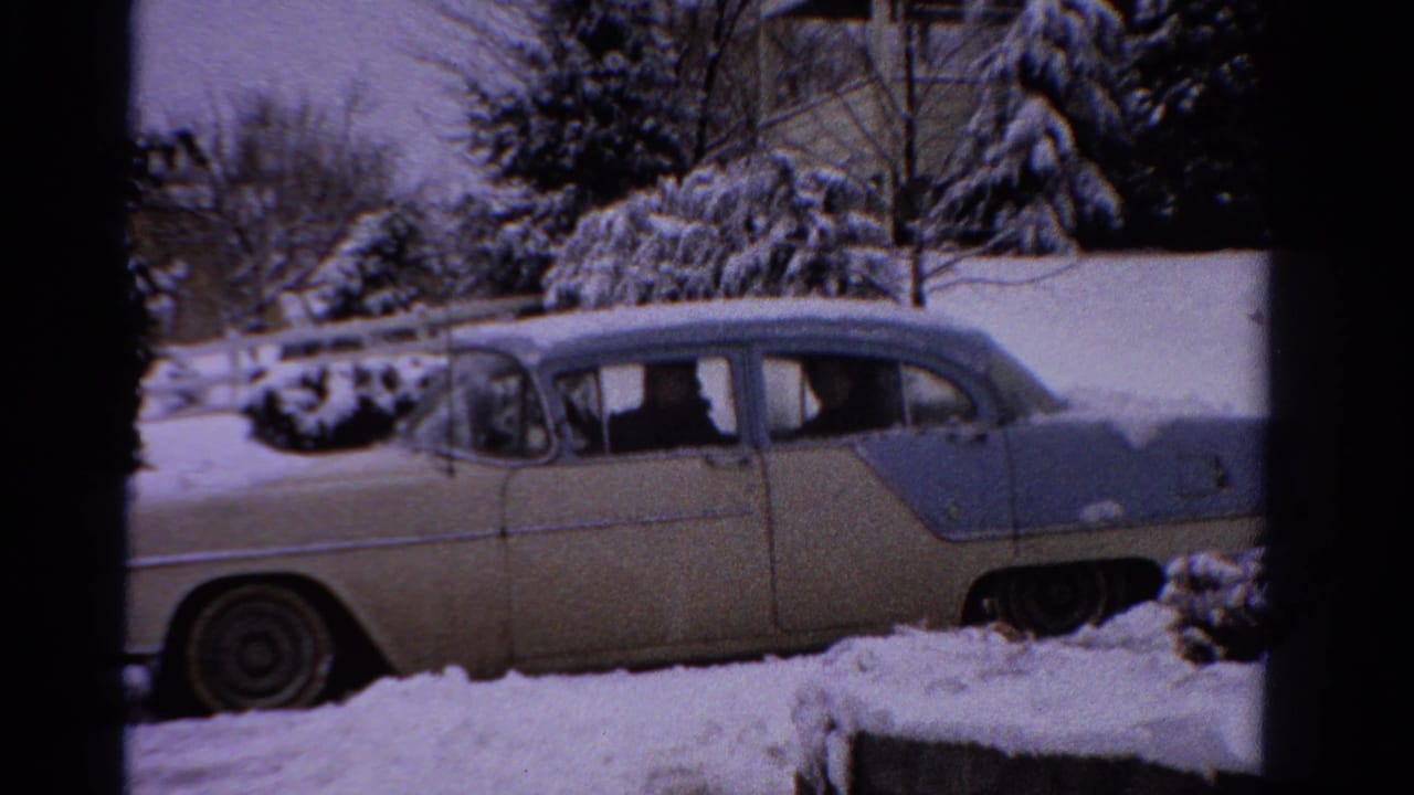 1958 Ontario winter frame showing a cream-and-blue mid-century sedan in snow with occupants visible through the windows.