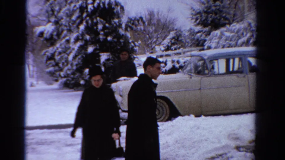 Adults in dark winter clothing move near a vintage sedan in a snowy Ontario residential setting, based on supplied metadata.