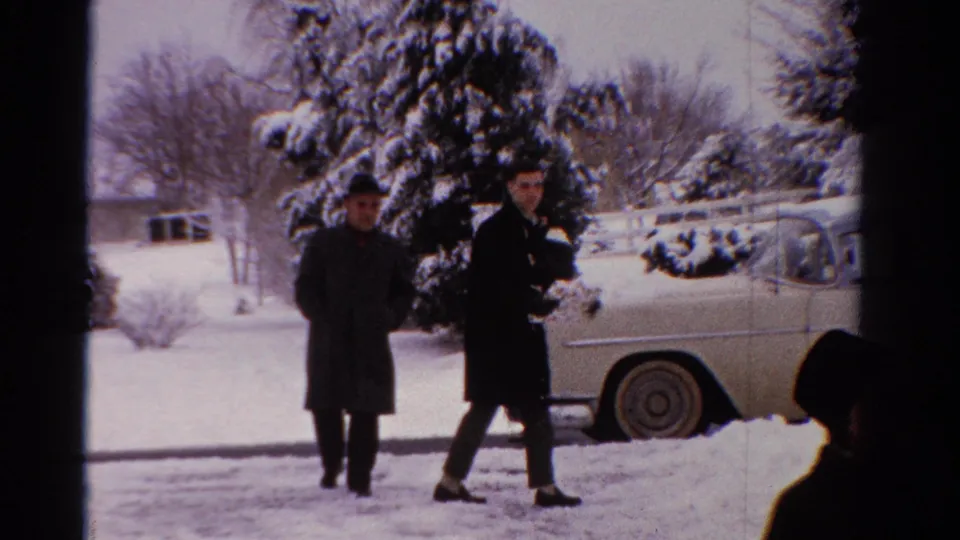 In the final frame, two adults stand in the snowy yard near the pale sedan, with one person holding a patterned box or parcel.