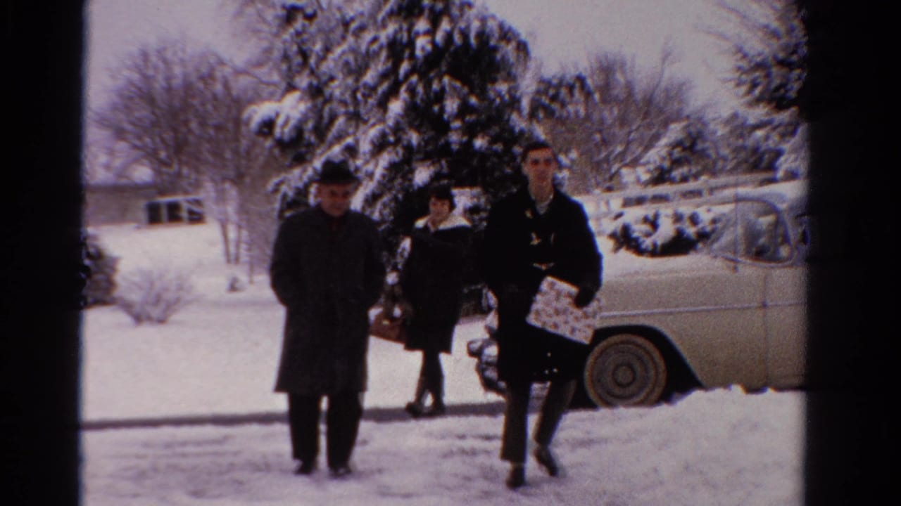 In 1958 Ontario home-movie footage, three adults in winter coats walk toward the camera through snow near a parked sedan.