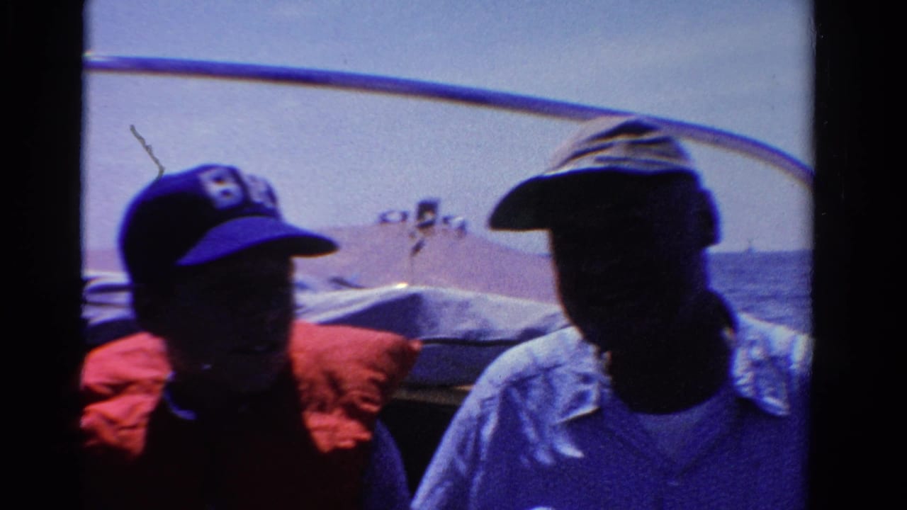 1958 Ontario 8mm frame showing two shadowed passengers seated in a small boat on blue water.