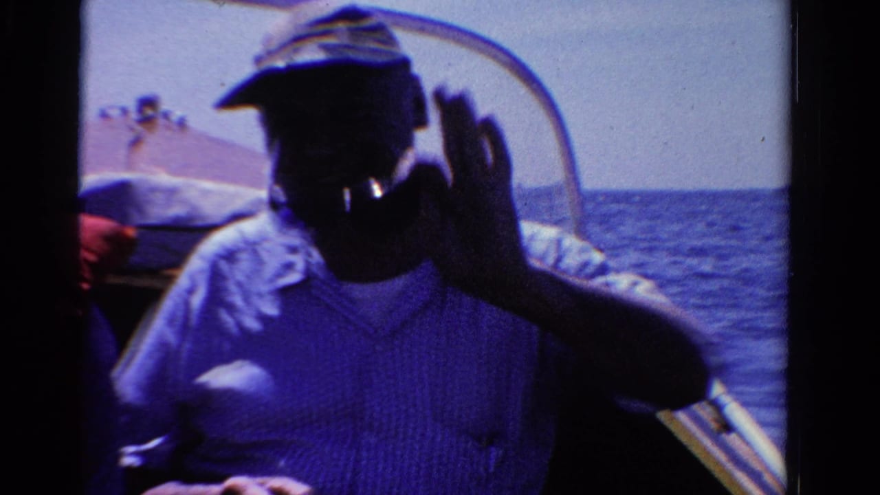 1958 Ontario home-movie frame of a man in a cap waving from a boat, with open water behind him.