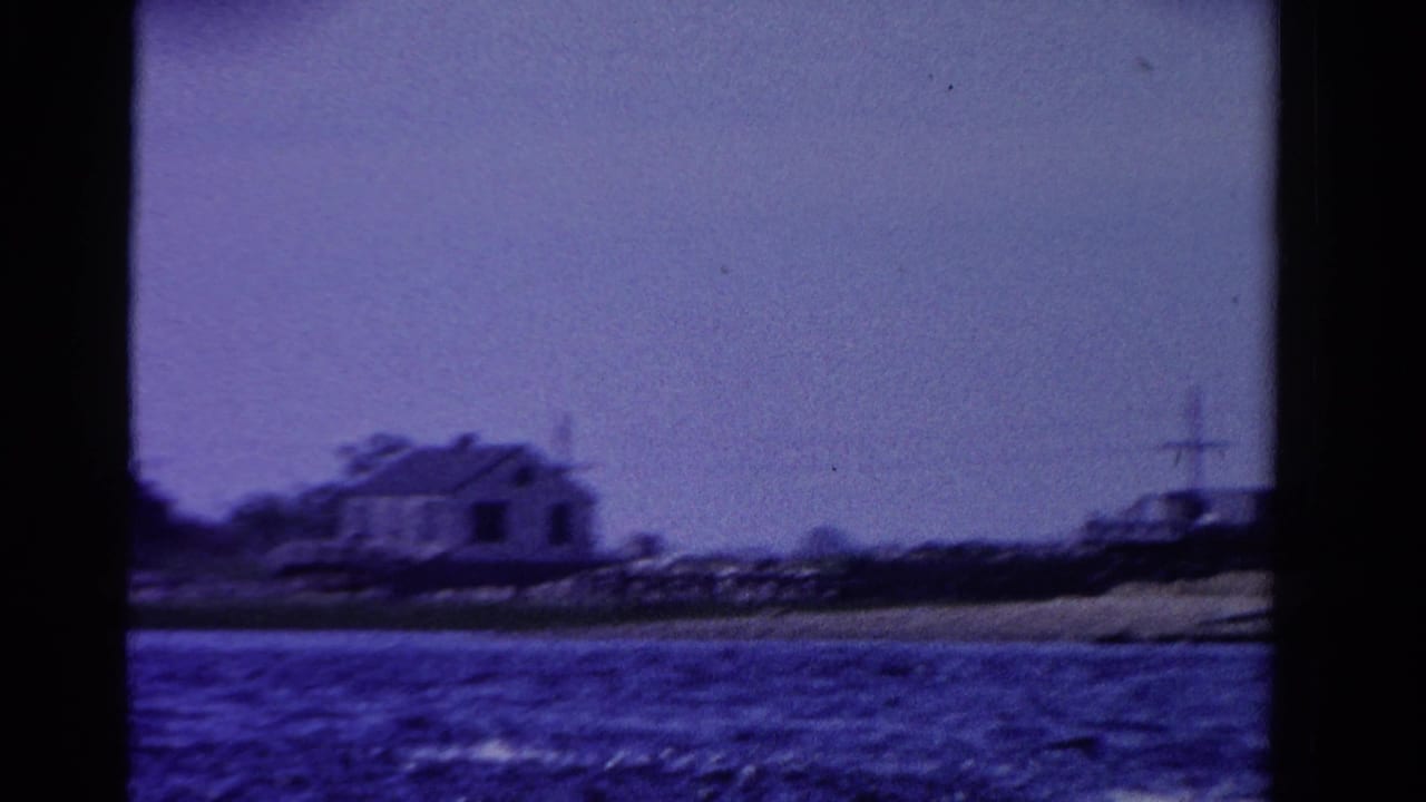 1958 Ontario 8mm frame showing a small shoreline house across blue water, with soft focus and visible film grain.