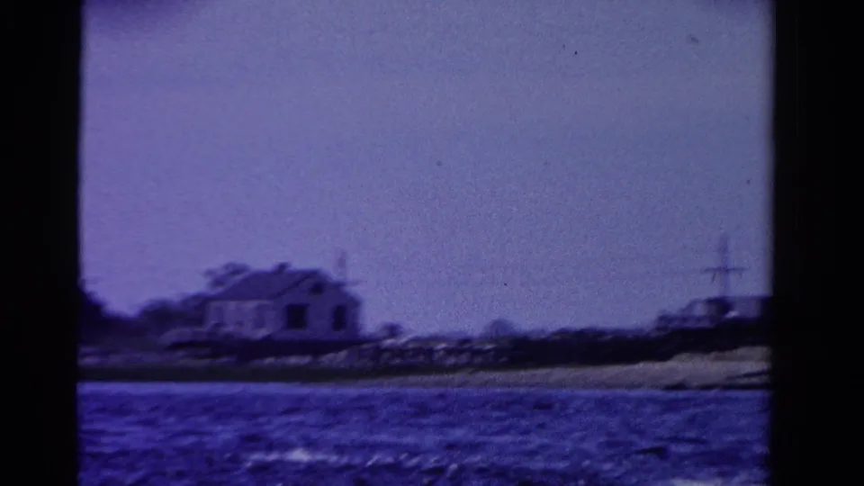 1958 Ontario 8mm frame showing a small shoreline house across blue water, with soft focus and visible film grain.