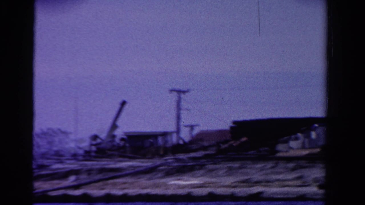 1958 Ontario waterfront view with low industrial buildings, utility poles, and shoreline equipment seen through aged 8mm color shift.