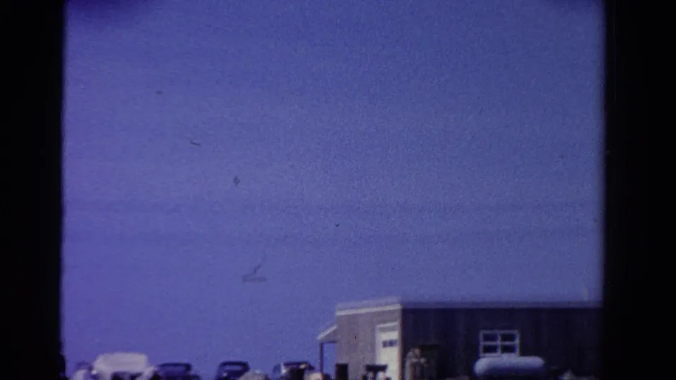 1958 Ontario streetscape with parked mid-century cars, a low building, and wide blue sky in a soft home-movie frame.