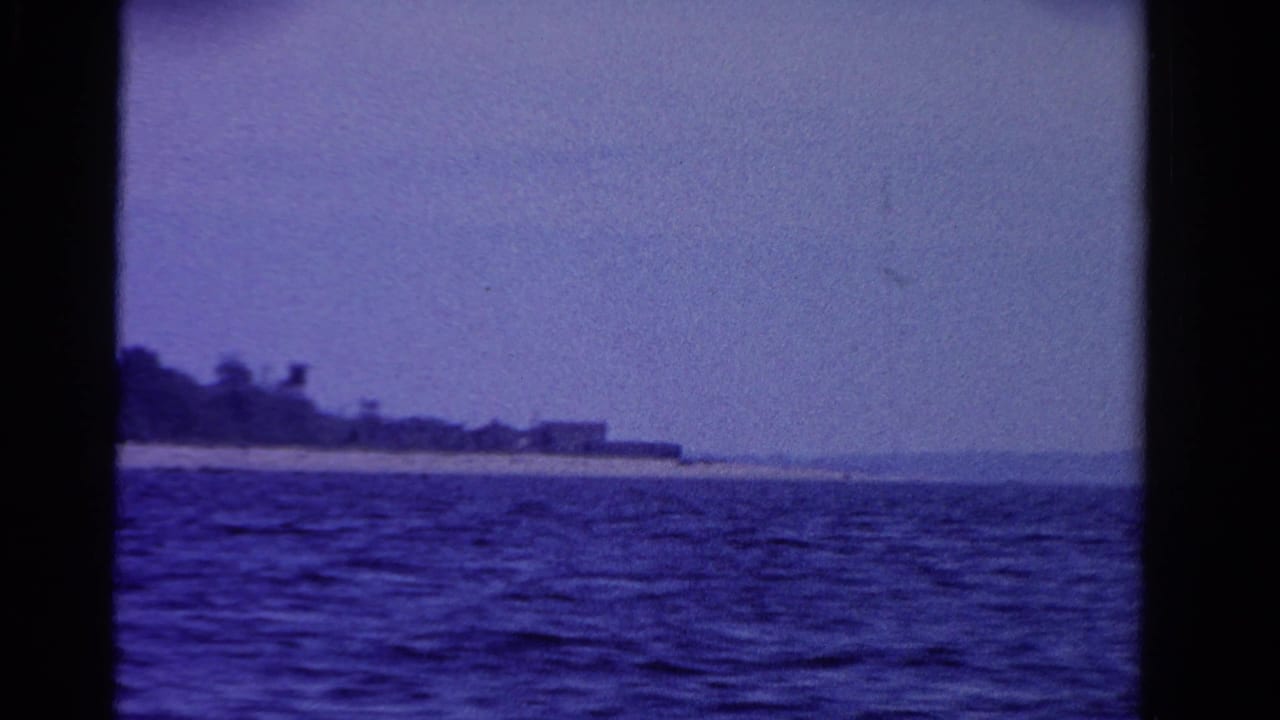 1958 Ontario 8mm frame showing lake water and a distant shoreline under a blue-purple film tint.