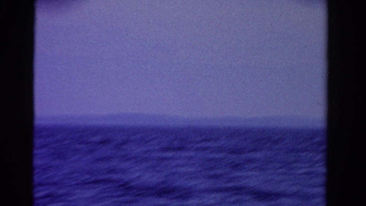 1958 Ontario home-movie frame of open water and a hazy far shore with strong blue-purple color shift.
