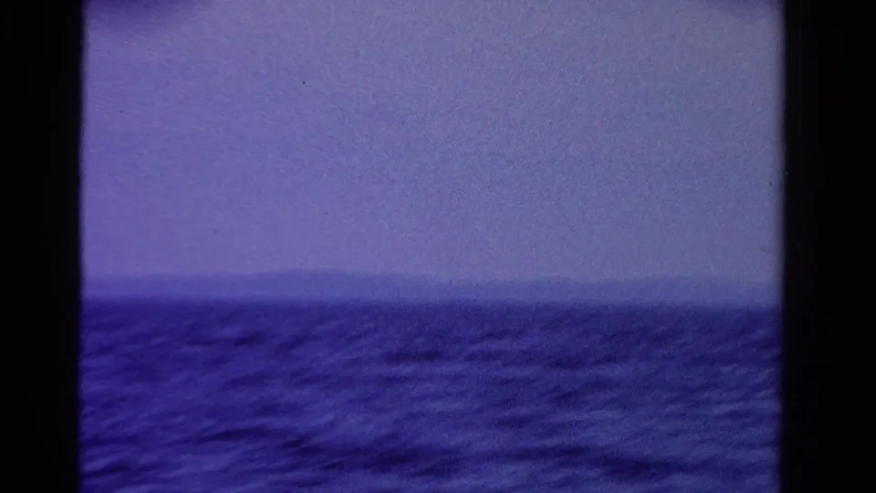 1958 Ontario home-movie frame of open water and a hazy far shore with strong blue-purple color shift.