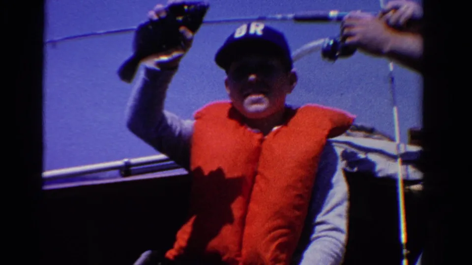 1958 Ontario boating frame with an adult fisherman holding up his catch, a rod at right, and lake water behind him.