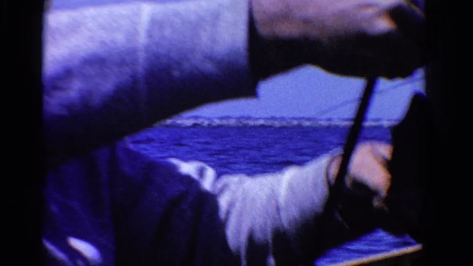 Close 8mm frame from the 1958 Ontario boat scene showing a cropped arm, fishing line, boat edge, and blue water beyond.