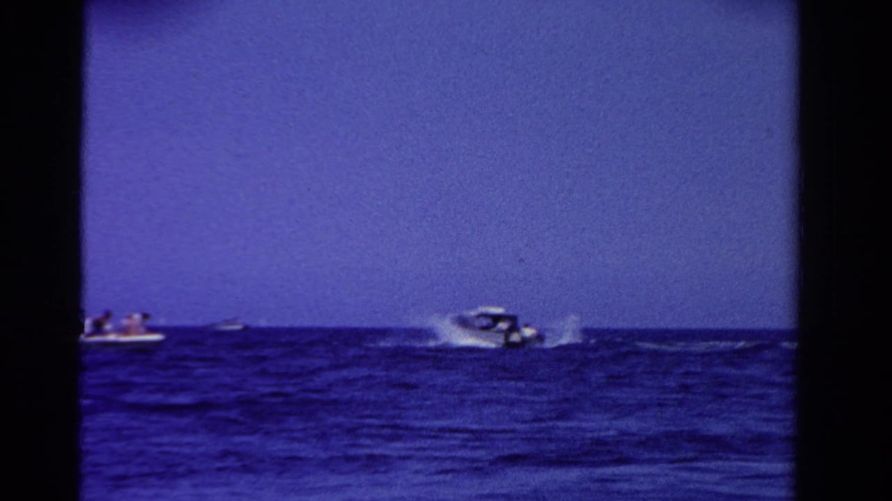 1958 Ontario home-movie frame showing distant speedboats crossing open blue water with white wakes behind them.