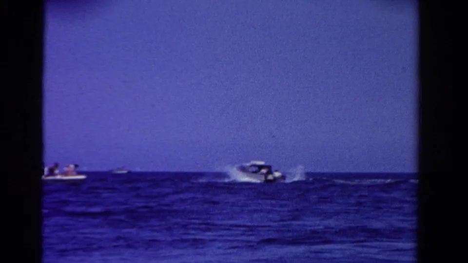1958 Ontario home-movie frame showing distant speedboats crossing open blue water with white wakes behind them.