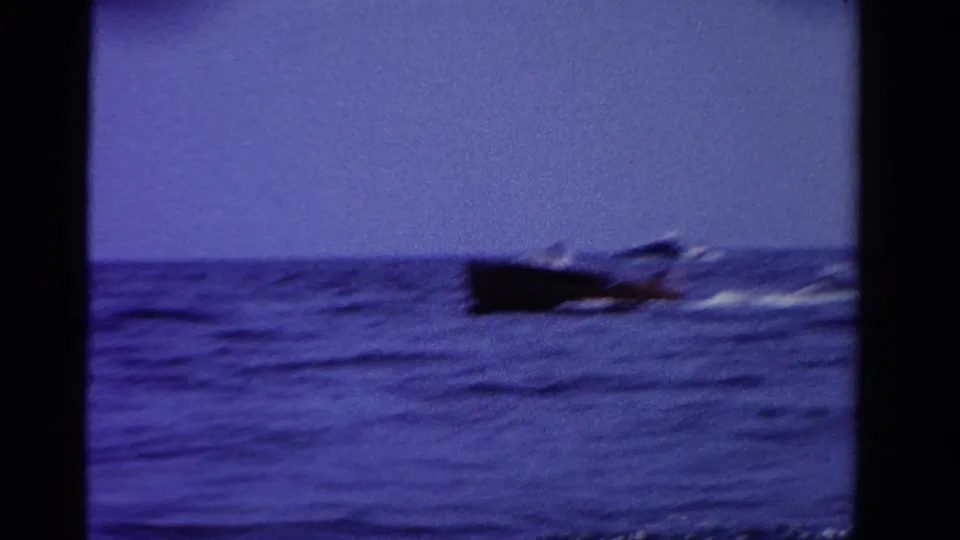 Close pass of a dark speedboat on Ontario water, captured with motion blur and grain in 1958 8mm footage.