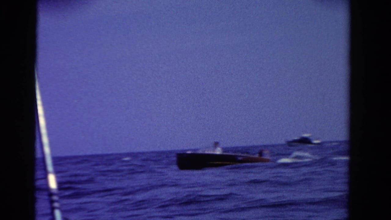 Dark motorboat crossing a blue lake with wake and a foreground pole.