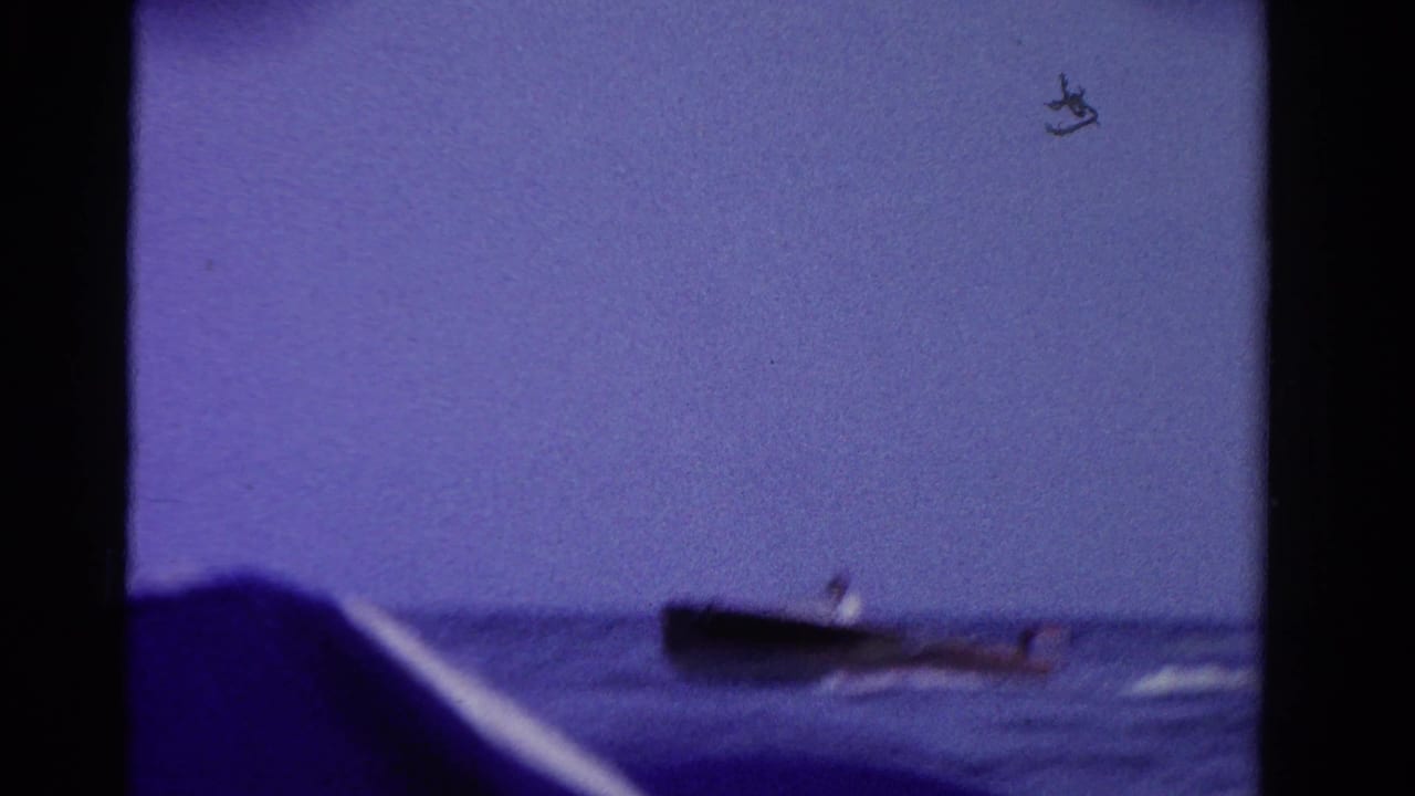 1958 Ontario 8mm home-movie frame showing a small motorboat crossing open lake water under a pale summer sky.