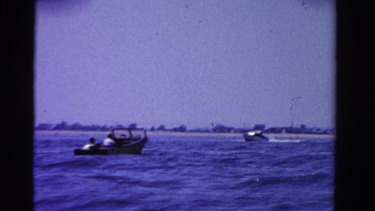 1958 Ontario lake scene with small motorboats and faint passengers visible against a low distant shoreline.