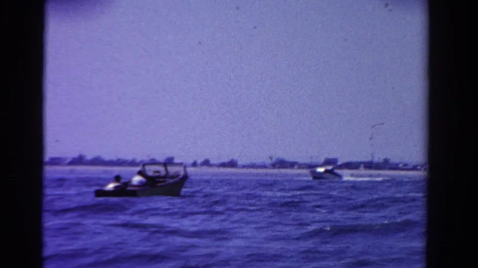 1958 Ontario lake scene with small motorboats and faint passengers visible against a low distant shoreline.