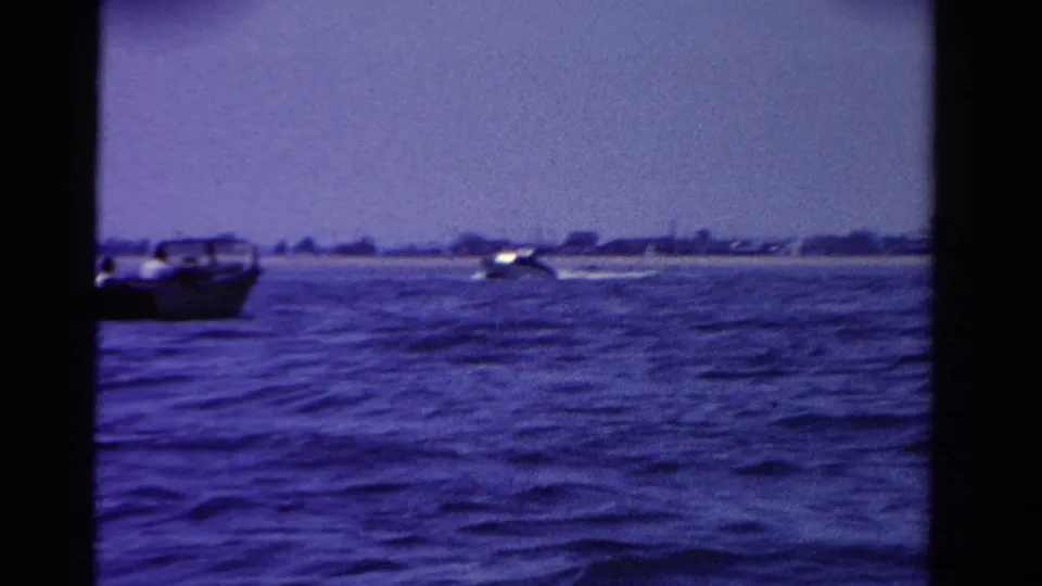 Blue-toned 8mm frame from Ontario in 1958 showing motorboats moving across a broad lake near a distant shore.