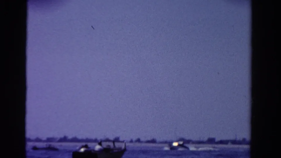 Wide 1958 Ontario home-movie view of a small motorboat near the bottom of frame with open water and distant shore beyond.