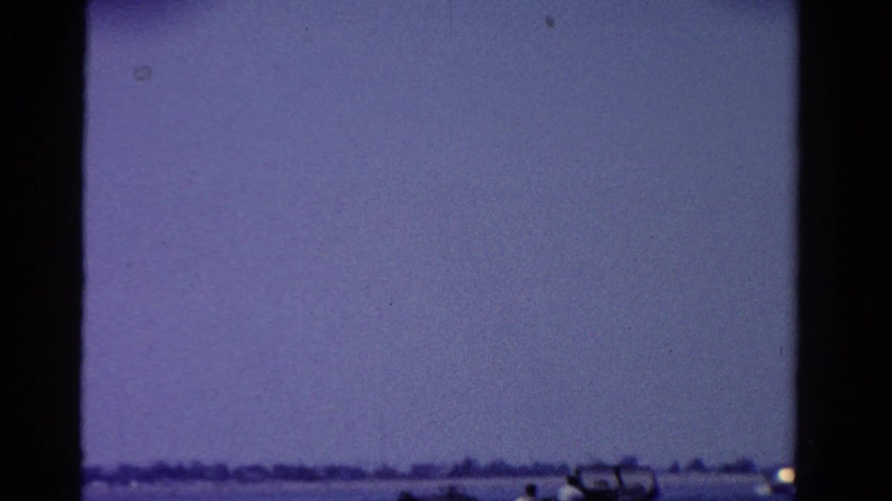 1958 Ontario home-movie frame with a hazy purple sky above calm water and a distant low shoreline.