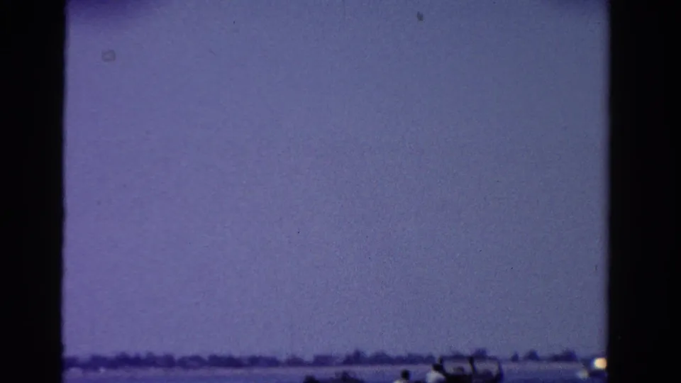 1958 Ontario home-movie frame with a hazy purple sky above calm water and a distant low shoreline.