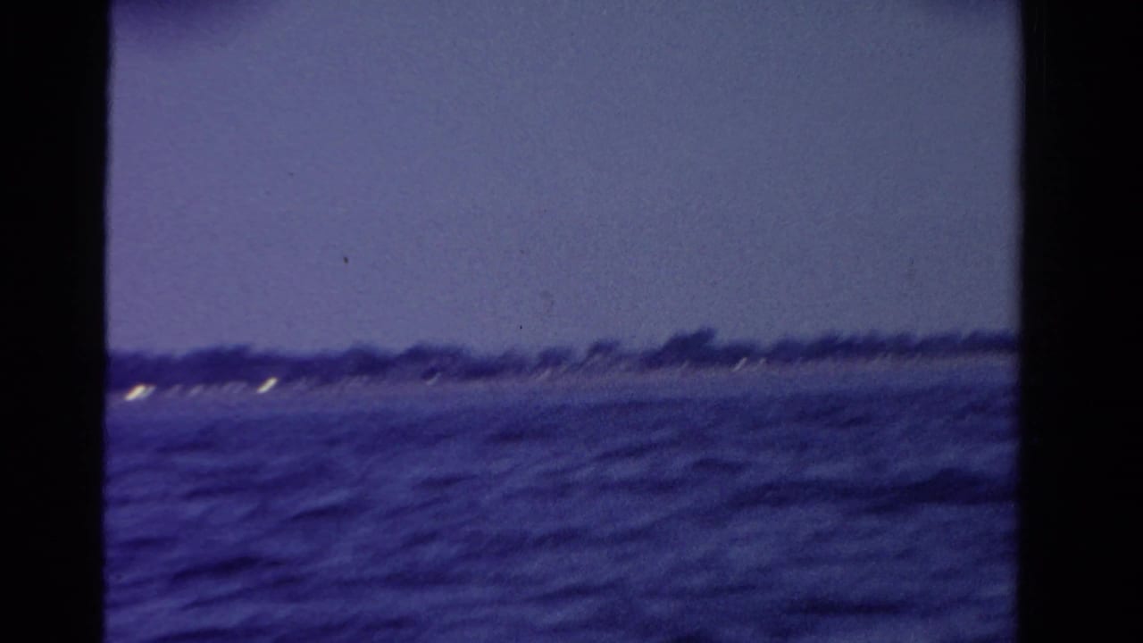 Dusk waterfront view in Ontario, with dark rippled water, a distant shoreline, and a few small lights.