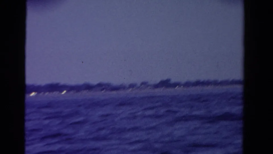 Dusk waterfront view in Ontario, with dark rippled water, a distant shoreline, and a few small lights.