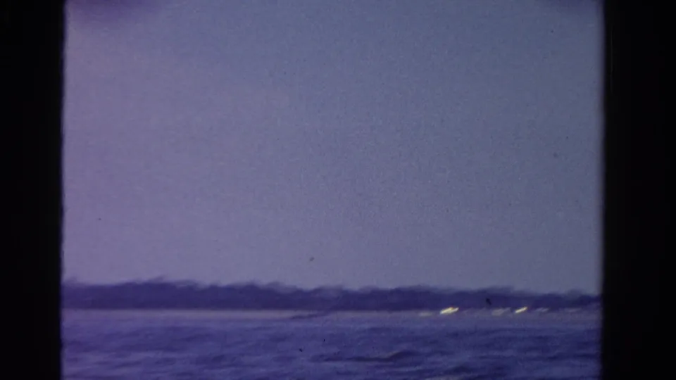 Soft 8mm view of an Ontario shoreline at dusk, with dark water, a hazy sky, and faint lights near the horizon.