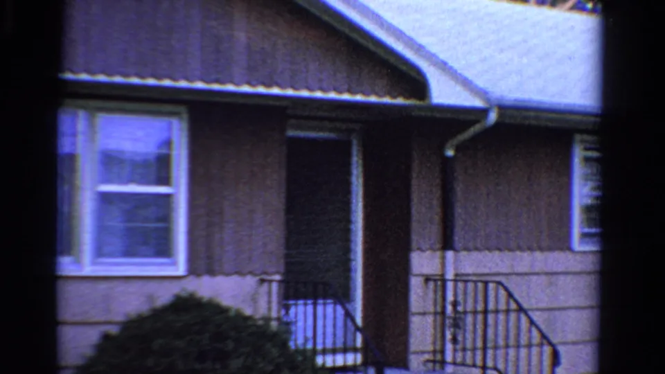 1958 Ontario 8mm still showing a suburban front entry, white-trimmed window, dark door, downspout, and metal railing.